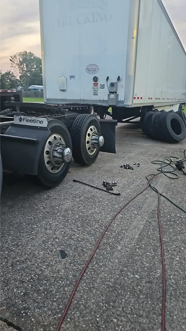 On-site Fleetline cargo trailer tire replacement with lug nuts and tools laid out on highway
