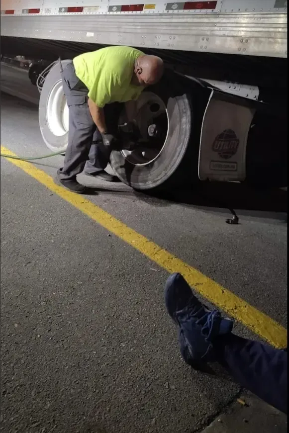 Night-time emergency tire repair on semi-truck trailer roadside in Arkansas